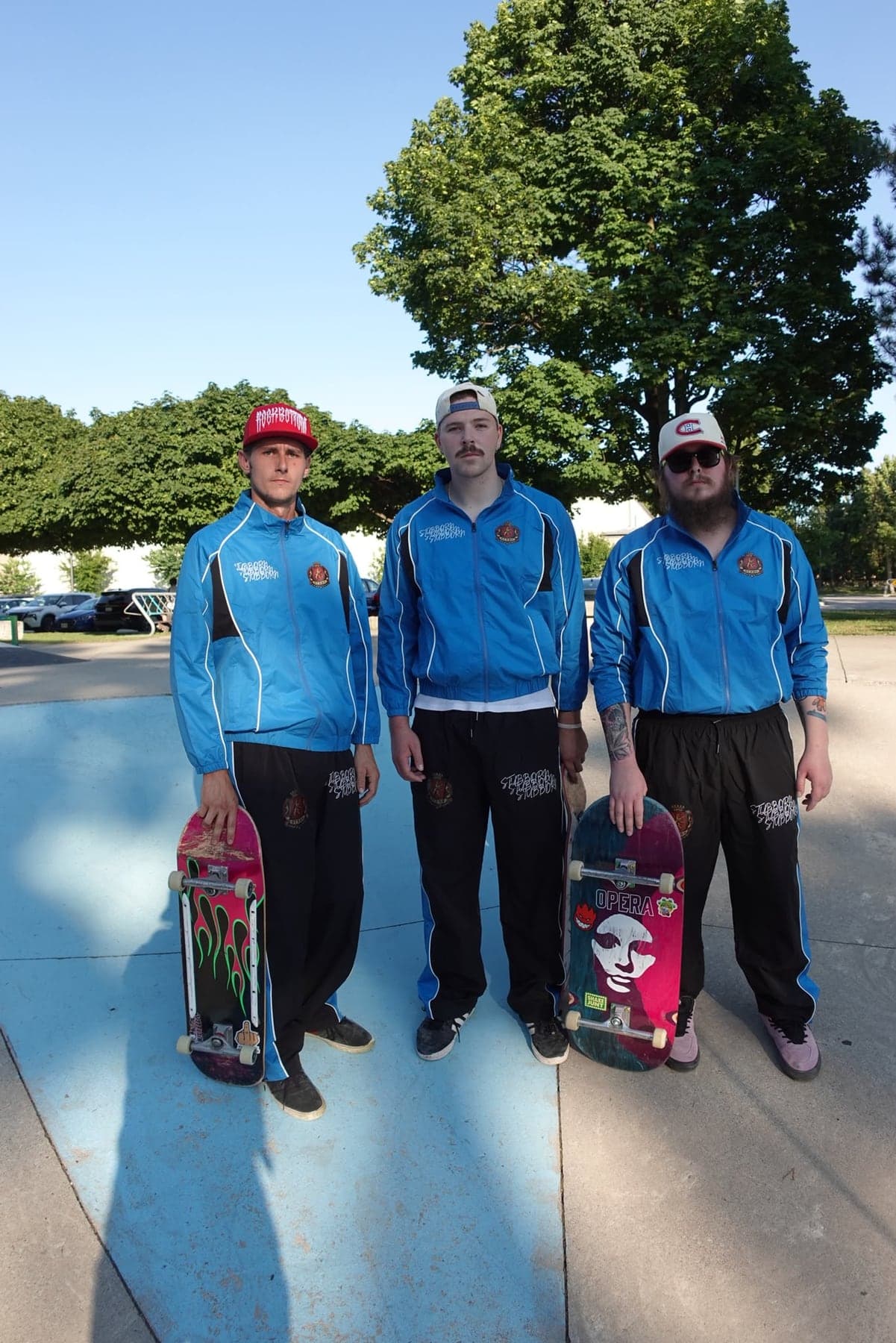 Three people standing at a skate park in the blue Stubborn Tracksuit