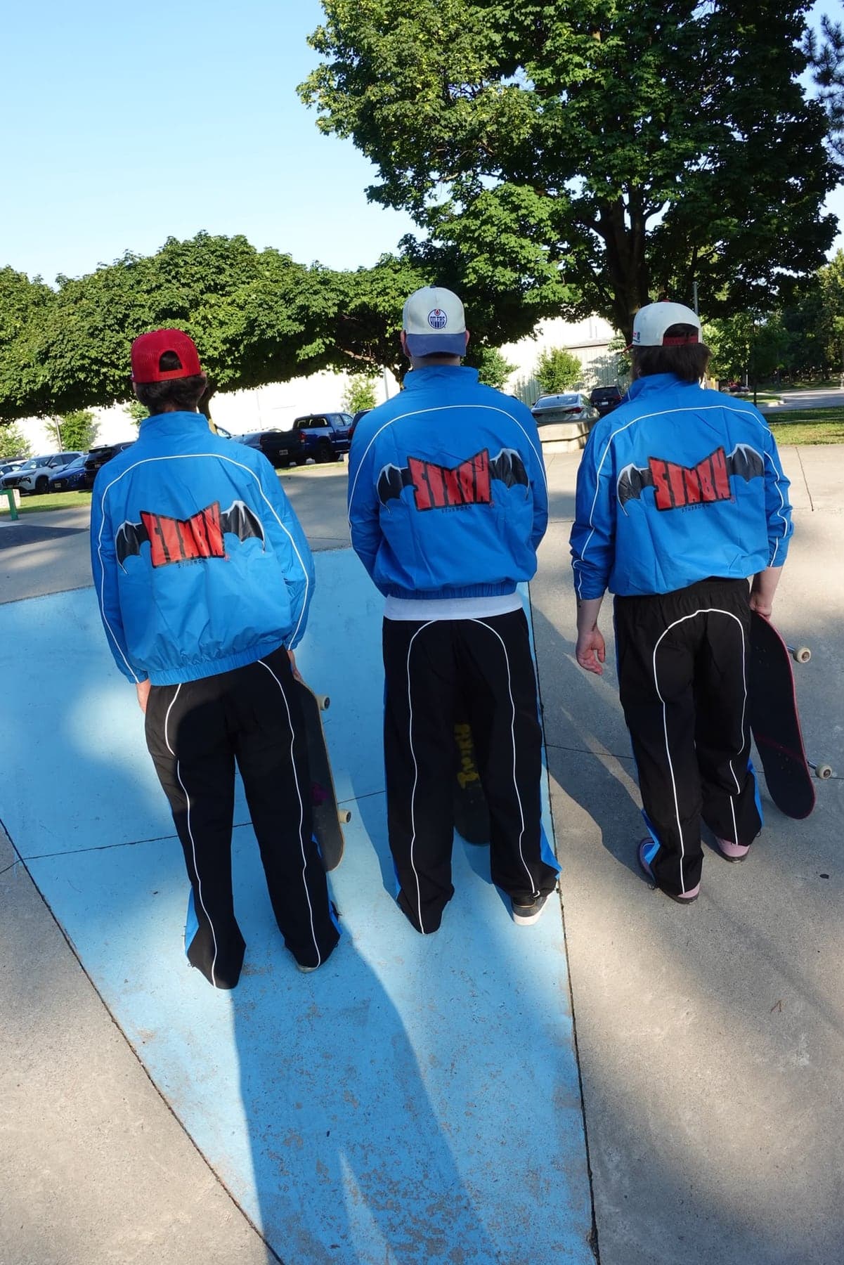 Three people seen from behind in blue Stubborn Tracksuit jackets with the STXBN wing logo across the back